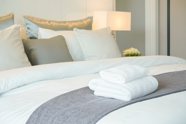 A close up of a bed with with white duvet covers and a grey throw and cushions